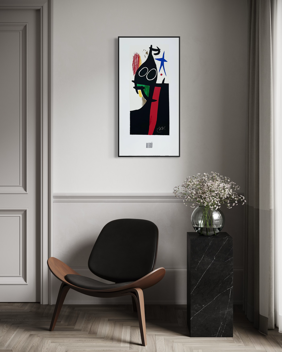A framed joan miro art print abstract art print hangs on a gray wall in a styled interior room with a black and wood chair, a black marble side table holding a vase of white flowers, and a doorway on the left.